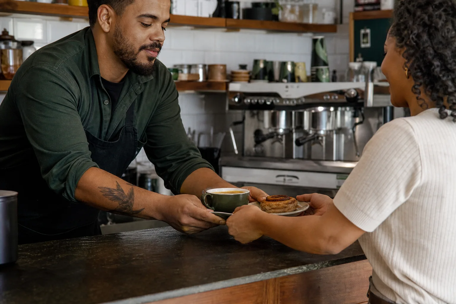 Barista entrega café e acompanhamento a uma cliente habitual no balcão